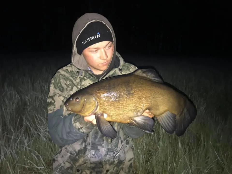 a fisherman holding a big male tench that he has caught at night