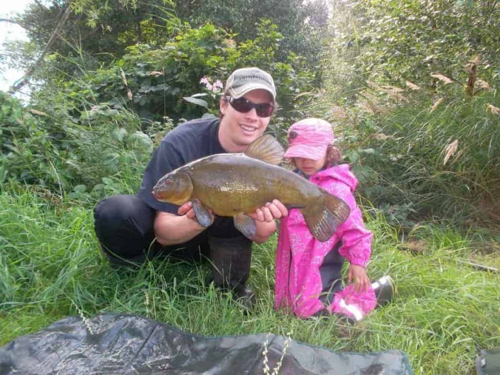 a fisherman with his daughter holding a big, fat tench that they have caught on sweetcorn