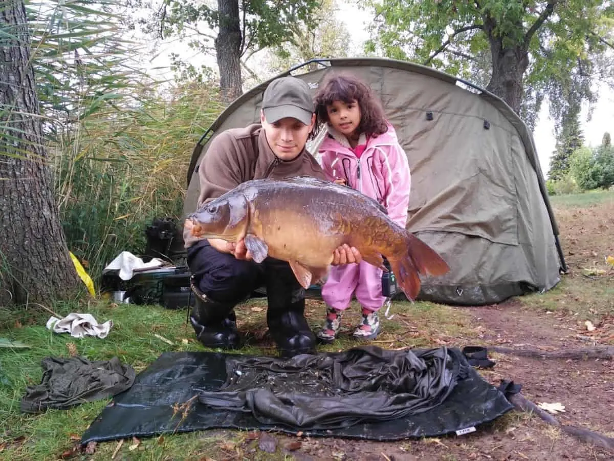 a carp angler and his daughter holding a fat mirror carp