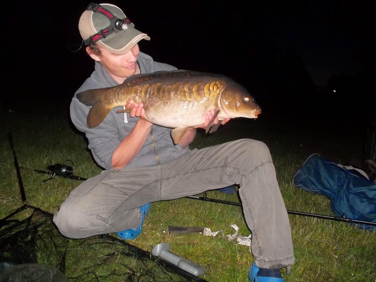 an angler fishing at night and holding a fat mirror carp