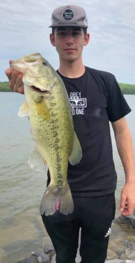 a bass angler holding a big largemouth bass that he has caught on a crankbait in muddy water