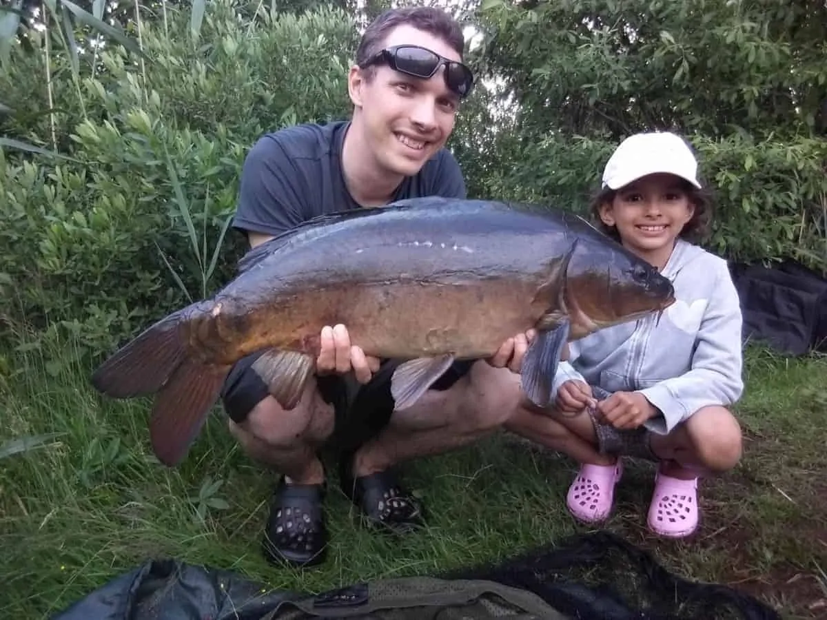 a carp angler with his little daughter holding a nice leather carp