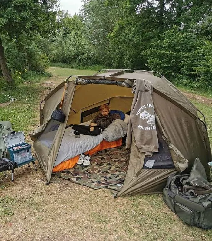 an open bivvy with a bed and fishing gear and a little boy in it