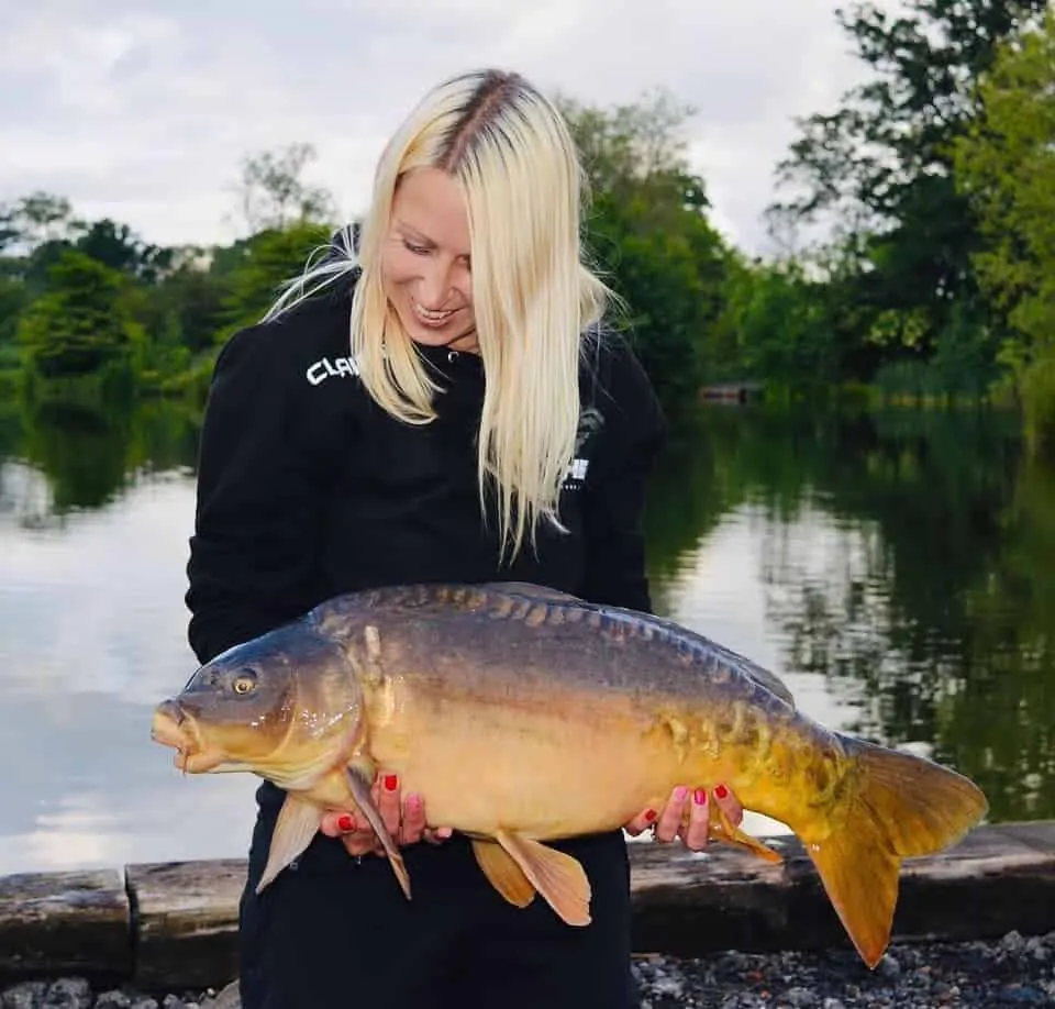 a female angler holding a beautiful mirror carp that she has caught on a bottom-rigged boilie.