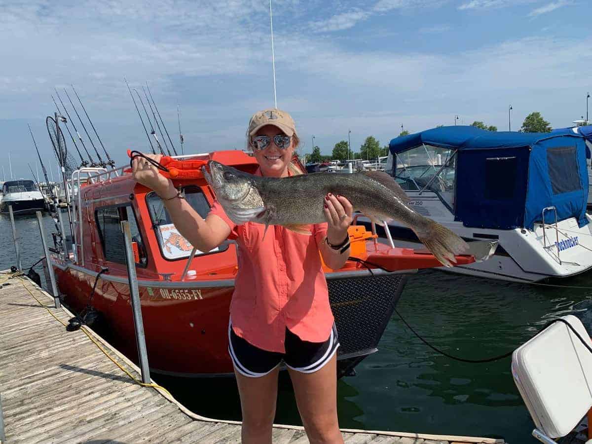 A female angler holding a large walleye in front of a boat.