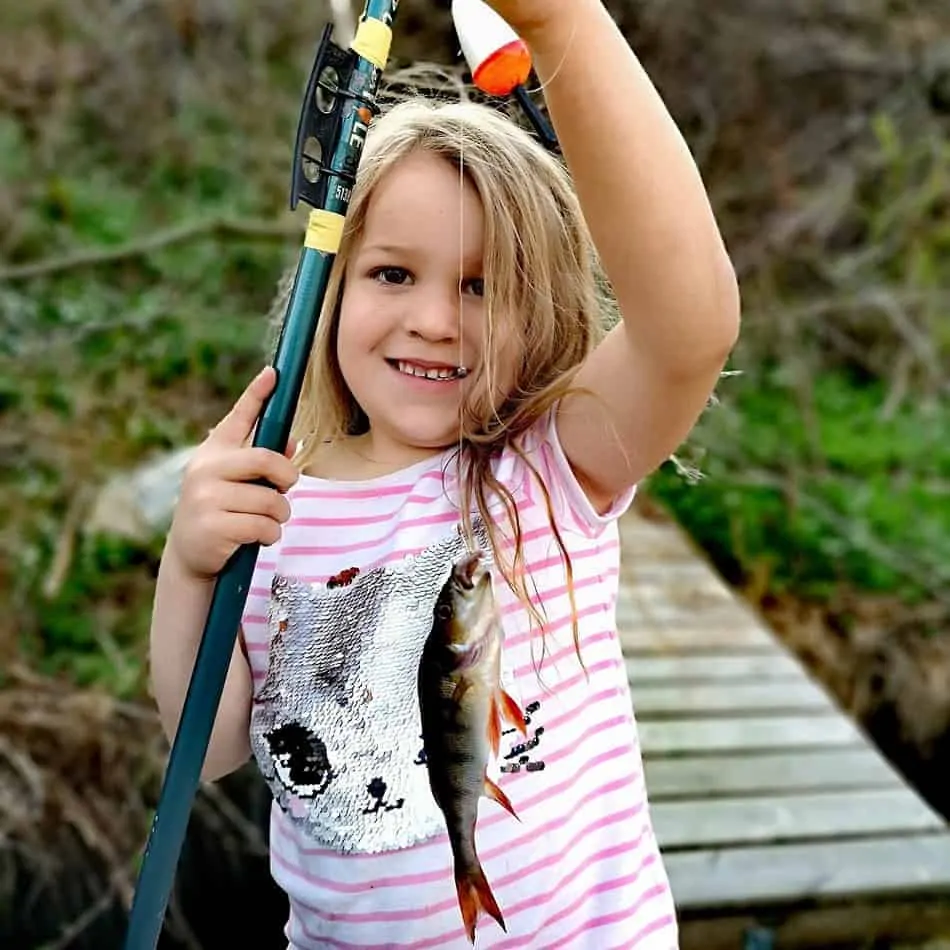 a little girl holding a fishing pole and a small perch