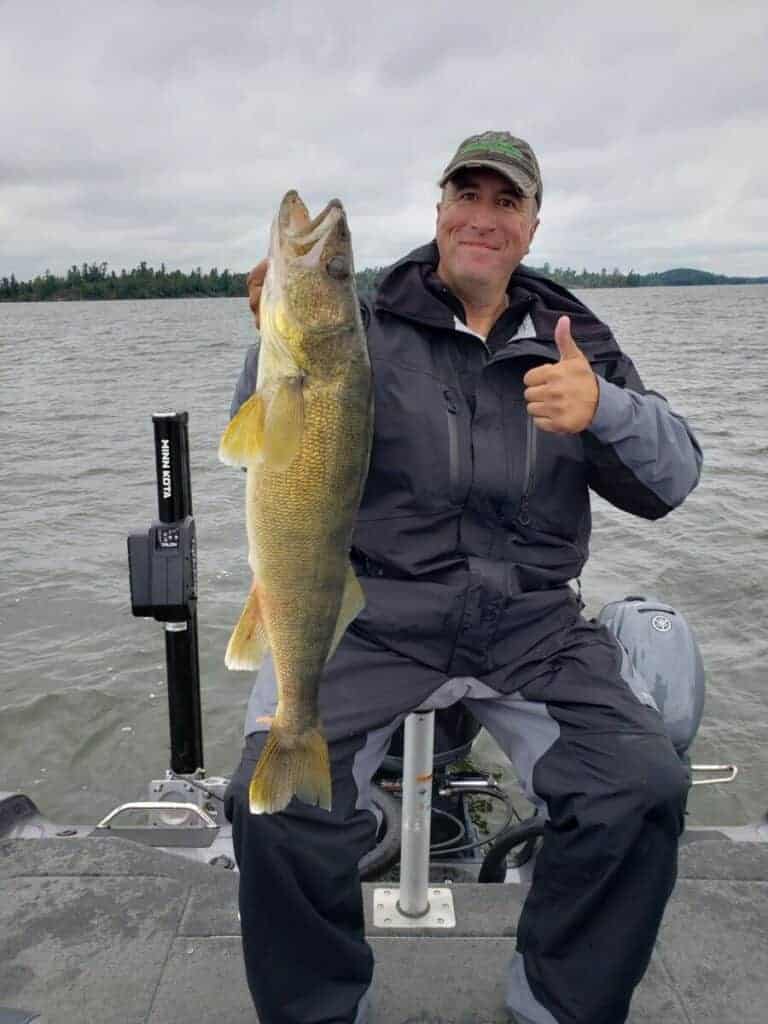 A fisherman with a huge walleye caught on a lake in cloudy weather.