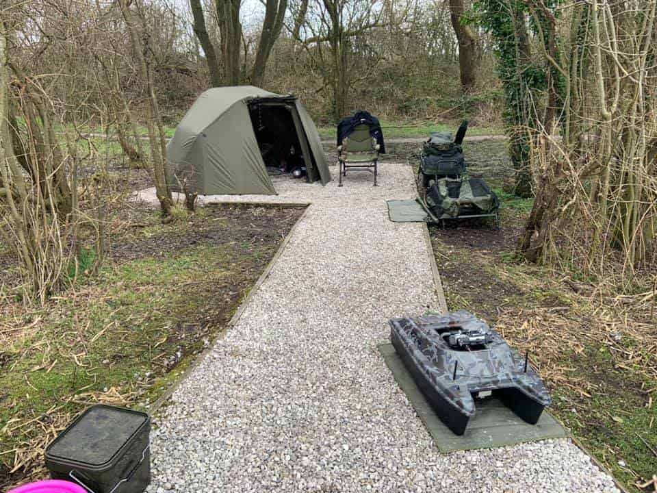 an image of a carp peg with a bivvy, a chair, fishing equipment and a bait boat