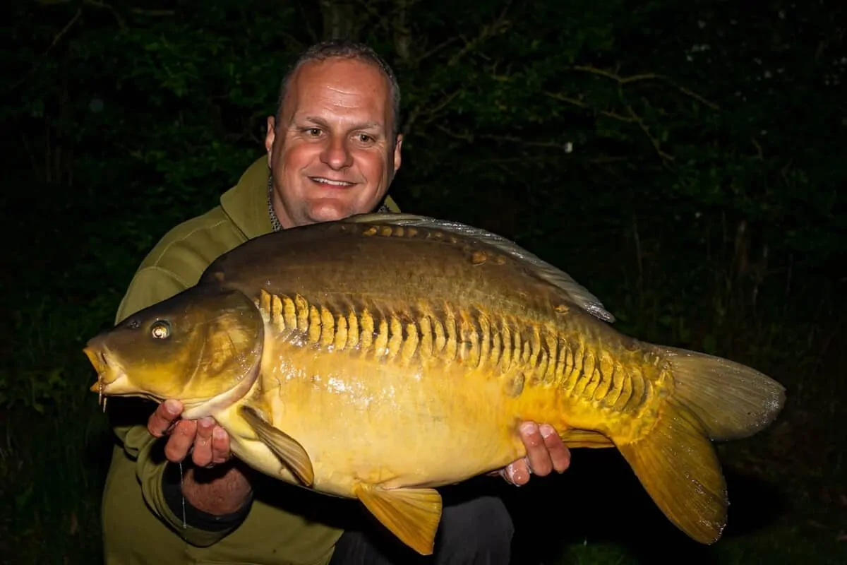 a carp angler holding a big linear carp that he has caught while night fishing