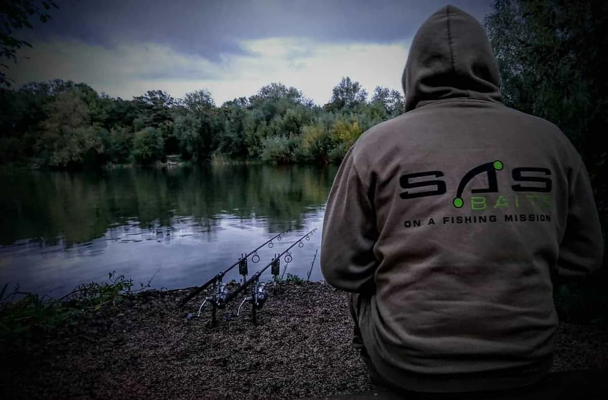 a carp angler sitting next to his rod pod with three carp rods on it waiting for a run