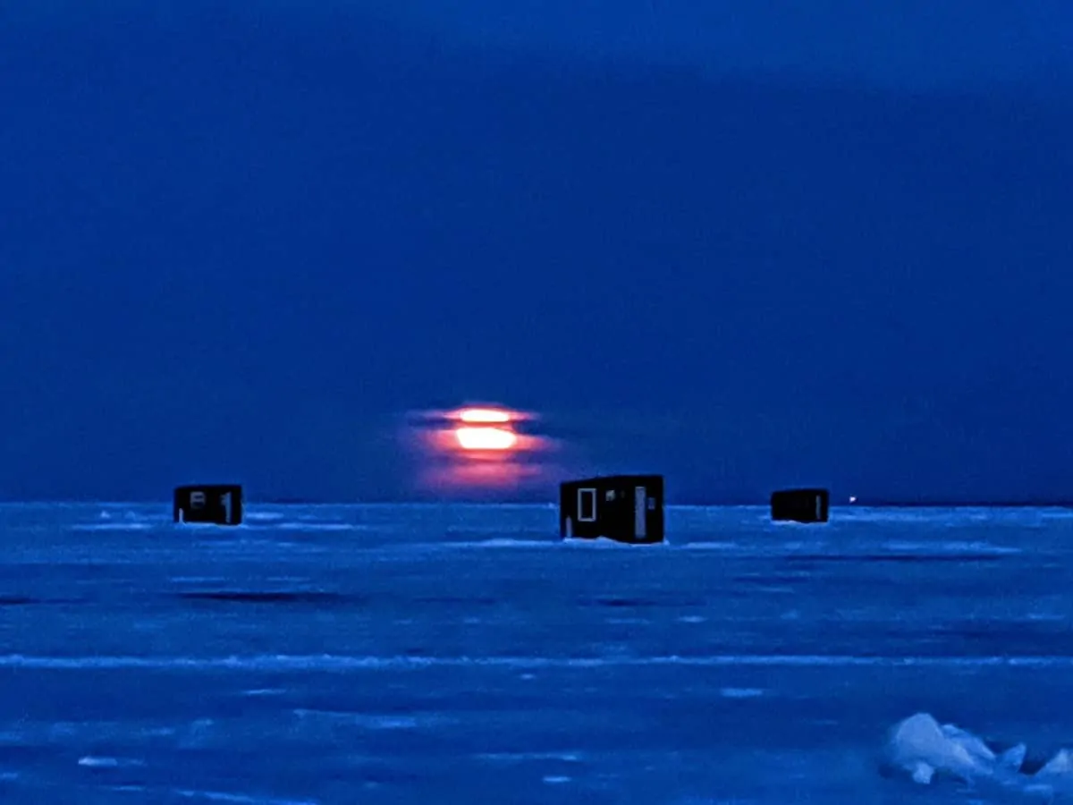 a picture of a frozen Minnesota lake by night with ice shacks on it