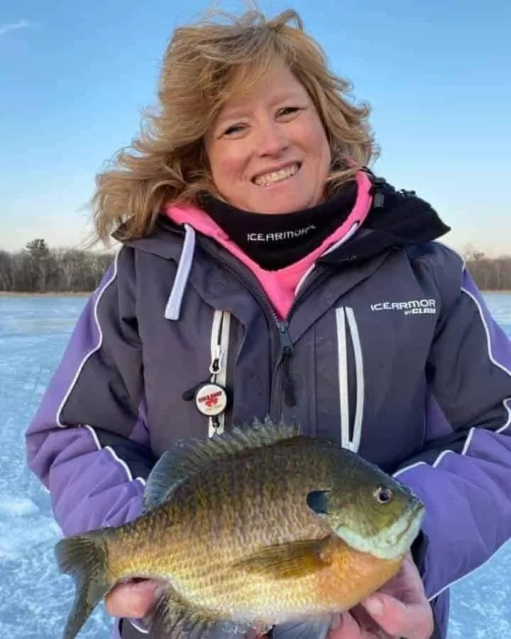 a female angler on a frozen lake in Minnesota holding a really big bluegill