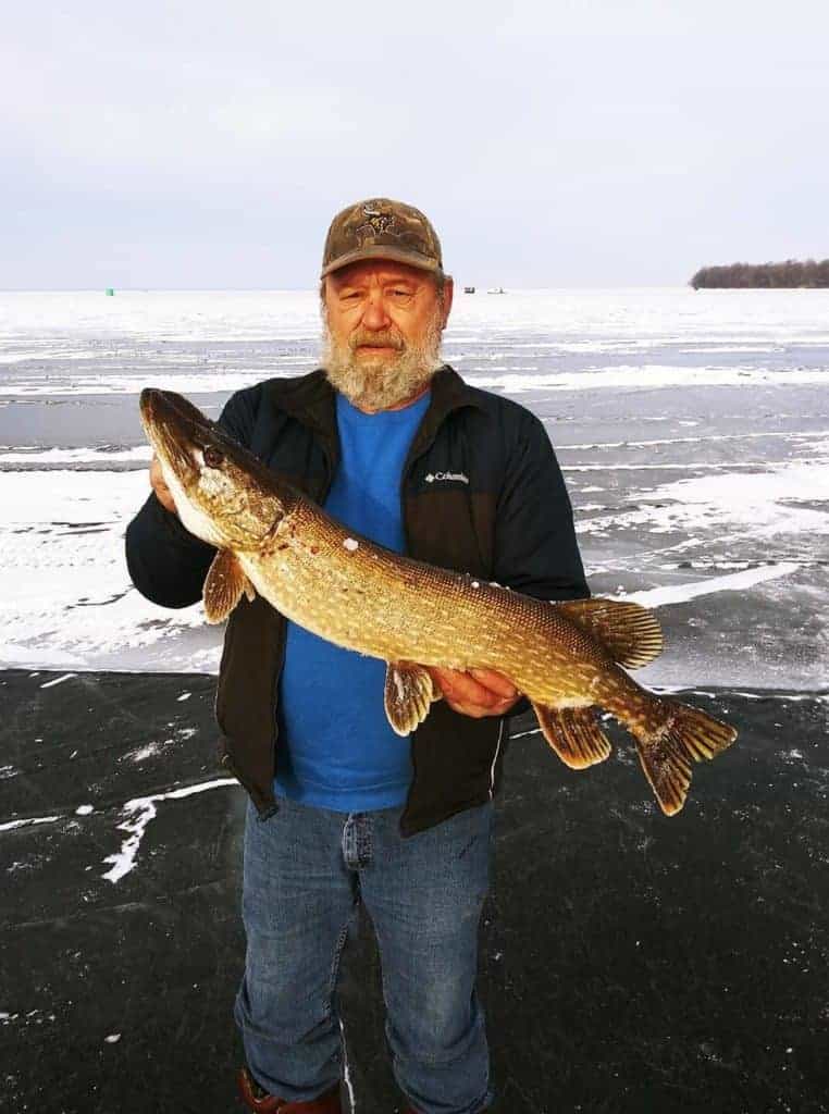an angler on a frozen lake in Minnesota holding a big northern pike