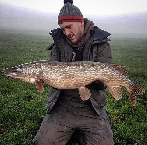 a happy angler with a fat pike that he has caught during a low pressure system on a local river
