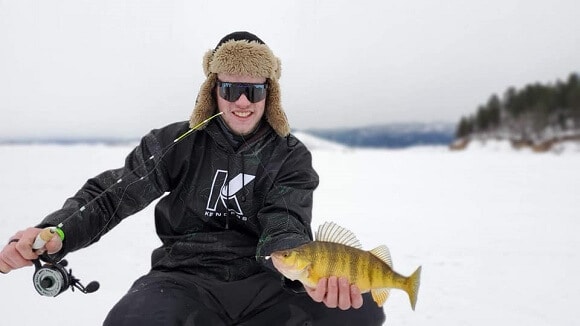 an ice angler on a lake holding a big yellow perch