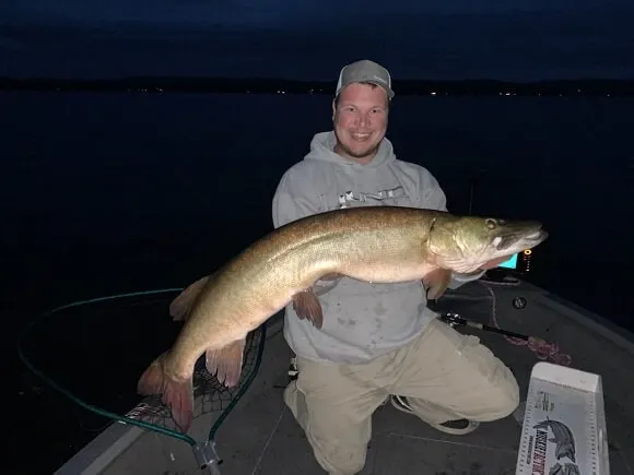 An angler holding a musky caught on a spinner bait in the middle of the night.