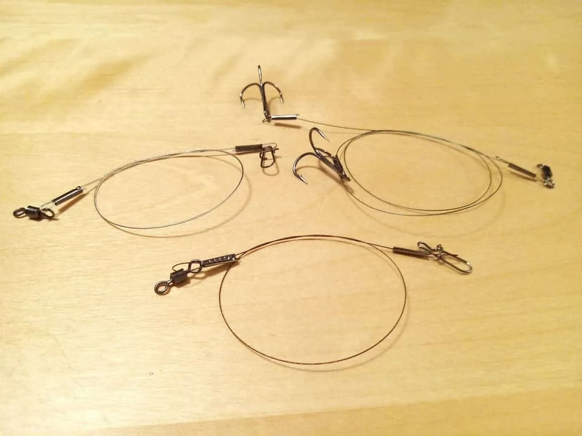 Homemade multi-strand steel leaders with treble hooks and swivels for lure and live bait fishing displayed on a table.