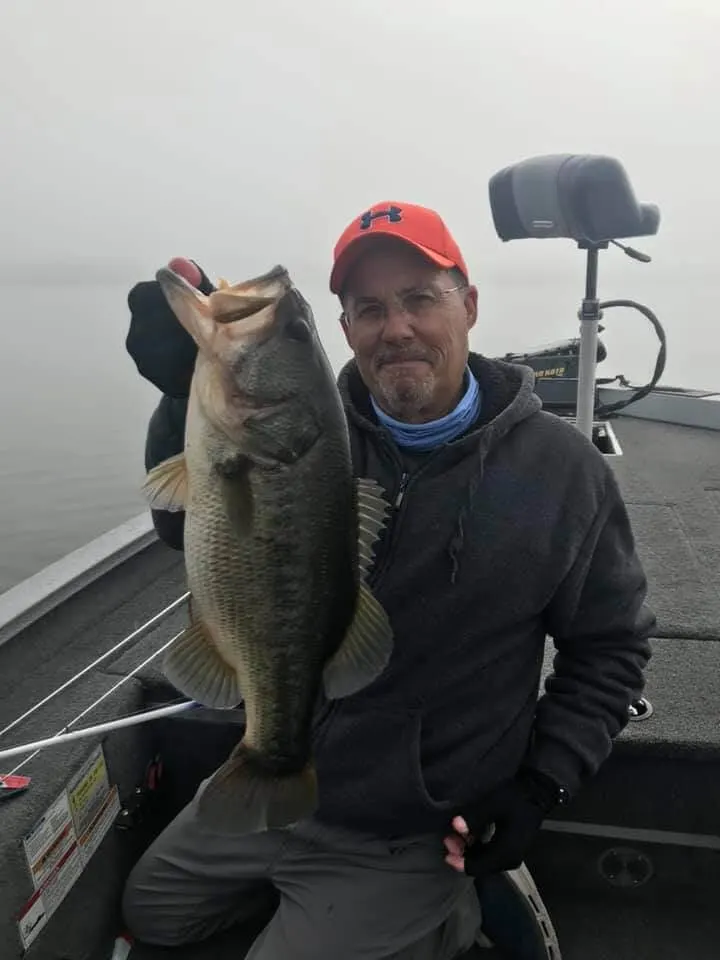 a happy angler holding a huge largemouth bass that he has caught on a crankbait from a boat.