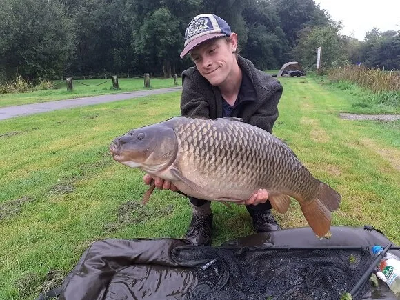 a happy carp angler holding a giant common carp over a beanie unhooking mat