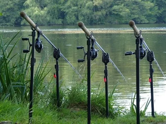 a set of three tench fishing rods on bank sticks with bite alarms and bobbins on the bank at a lake