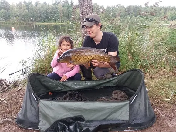 a carp angler and his daughter holding a common carp and using a carp cradle to handle the fish correctly.