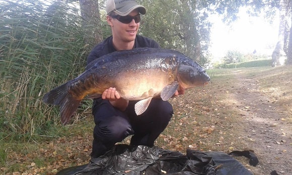 a carp angler holding a huge mirror carp that he has caught on the hair rig