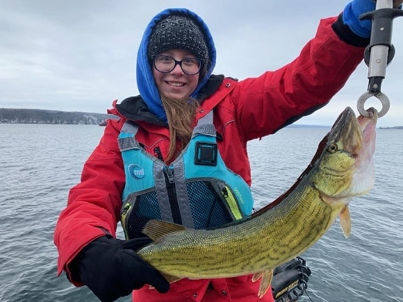 a happy female angler on a boat holding a nice pickerel that she has caught on a minnow spoon