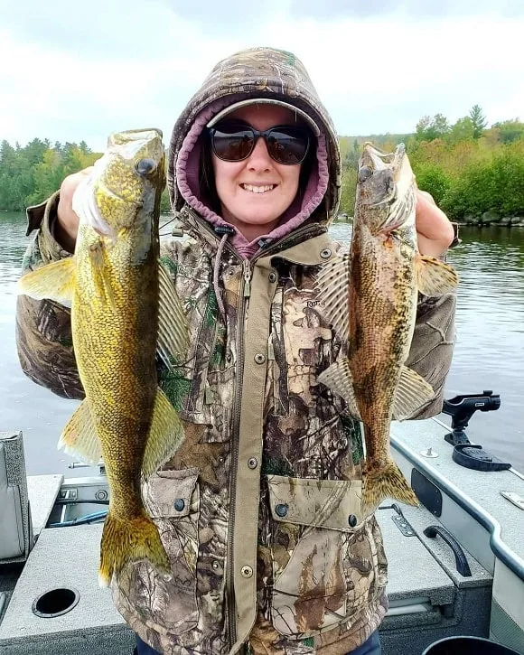 a female angler on a boat holding a walleye and a sauger that she has caught on a small crankbait