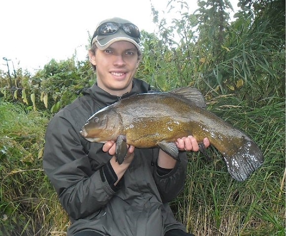a fisherman holding a very big tench that he has caught in autumn 