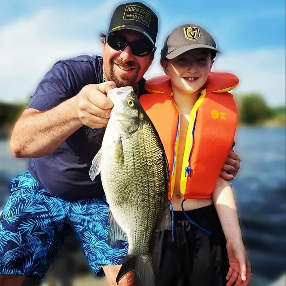 a fisherman and a young kid on a boat holding a white bass that they have caught on a small crankbait