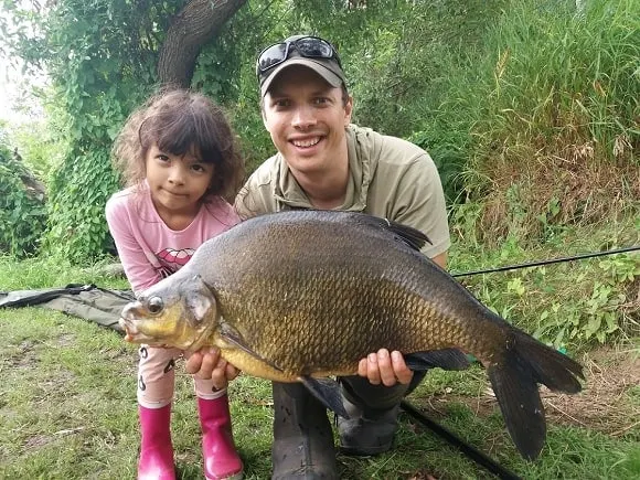 a coarse angler and his daughter with a huge common bream caught over a bed of groundbait and sweetcorn