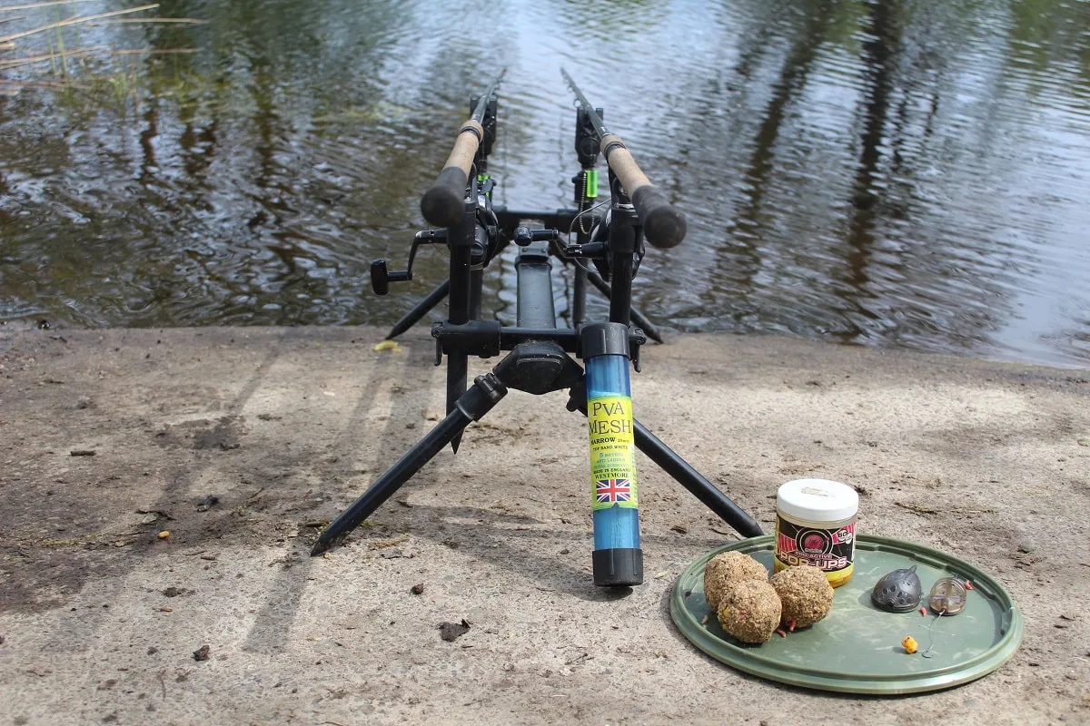 two specialist rods for tench on a rod pod with some groundbait, method feeders and pop-ups next to it