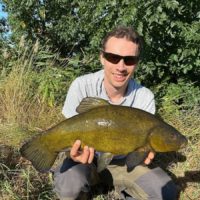 a fisherman with a big tench that he has caught in the middle of summer