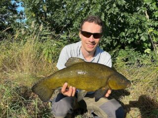 a fisherman with a big tench that he has caught in the middle of summer