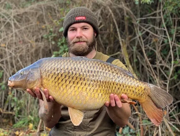 a carp angler holding a big common carp that he has caught on a boilie and pop-up