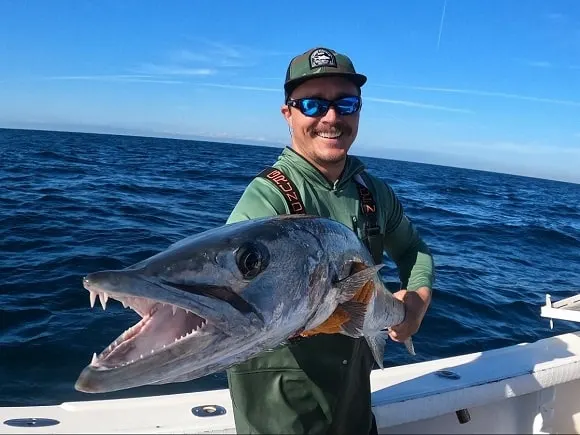 a happy saltwater angler on a boat holding a toothy barracuda