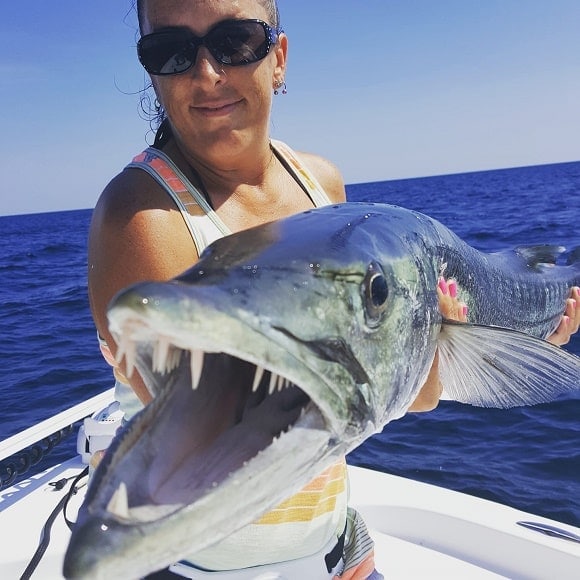 a saltwater angler on her boat with a big barracuda showing its teeth