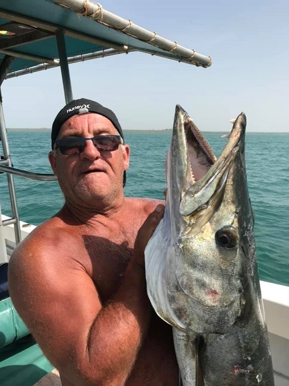 a fishing guide on his boat holding a large barracuda showing its teeth