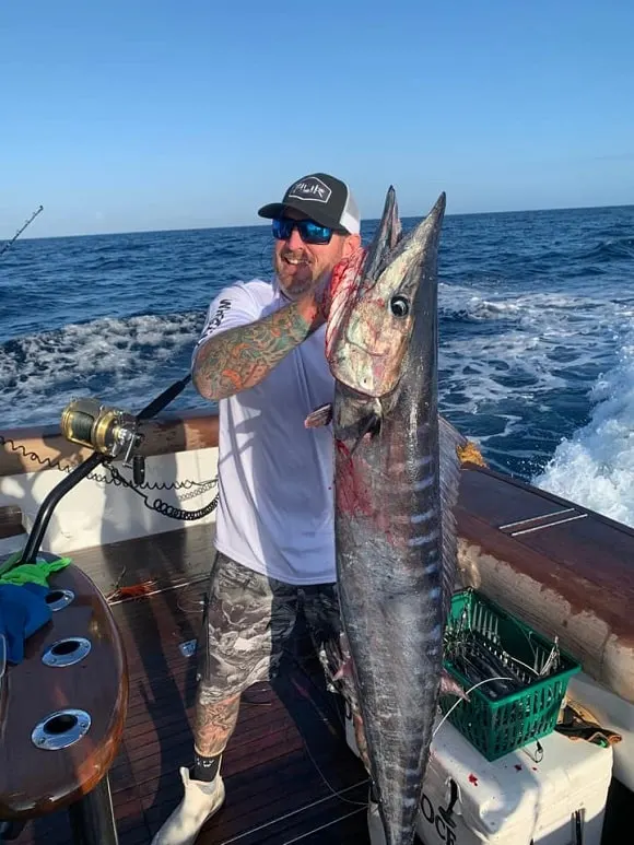 a fisherman on a boat on the ocean holding a large wahoo