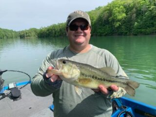 a bass angler on his boat holding a big largemouth bass that he has caught on a fluorocarbon leader and a small crankbait