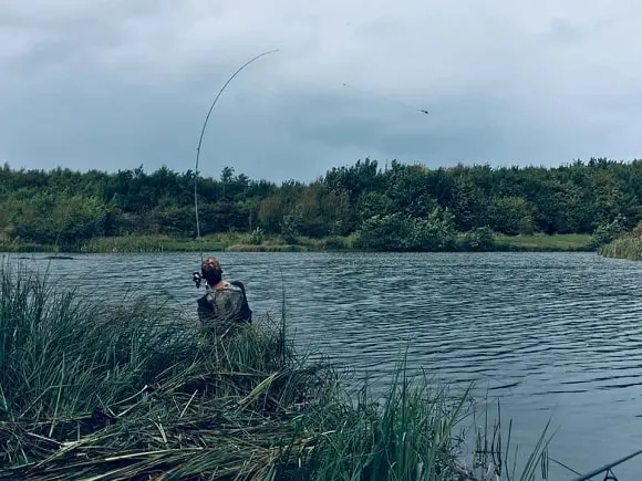 a carp angler casting out a rod on lake in windy conditions