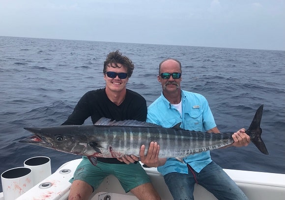 2 saltwater fishermen on a boat holding a big wahoo caught on a steel leader and a wahoo trolling lure