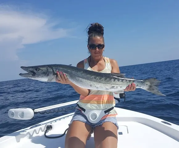 a female angler on a boat with a big barracuda that she has caught on a crankbait
