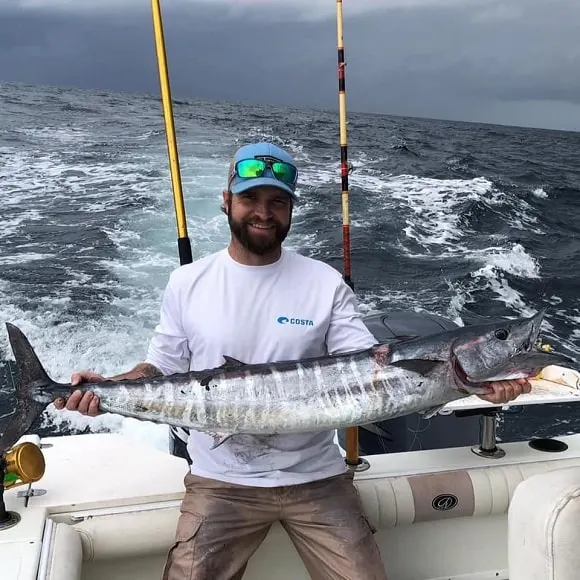 a saltwater fisherman on a boat holding a big wahoo that he has caught on a trolling wahoo lure