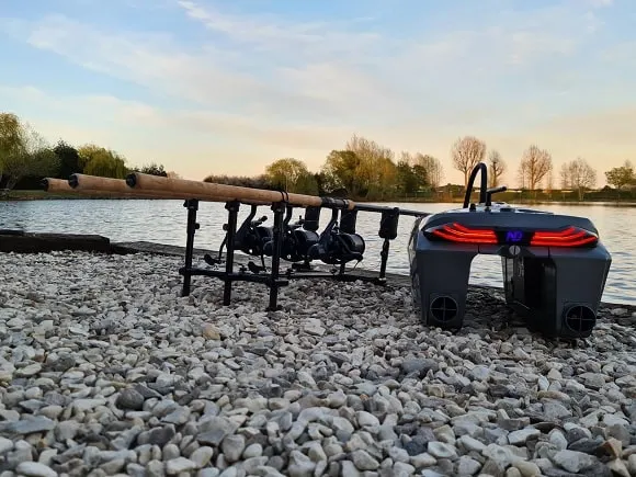 a bait boat on the bank next to a rod pod with three carp fishing rods