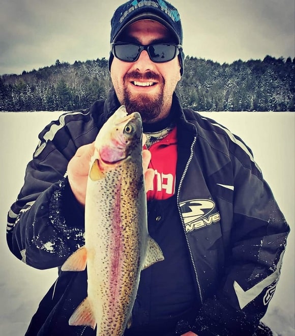 an ice angler on a frozen lake holding a smaller rainbow trout