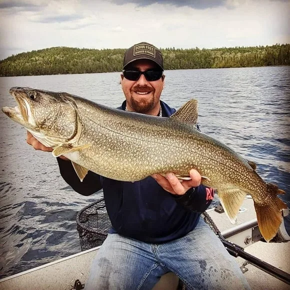 a fisherman on his boat holding a giant lake trout that he has caught vertical jigging