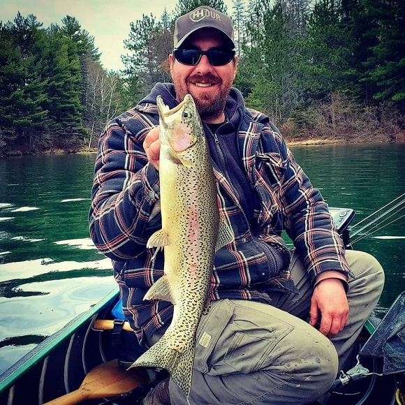 a fisherman on his boat holding a beautiful rainbow trout that he has caught on a slip bobber rig and a small minnow