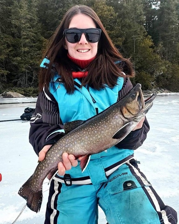 a female ice angler holding a long and dark brook trout