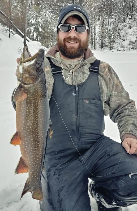 a fisherman on a frozen lake holding a giant splake that he has caught ice fishing